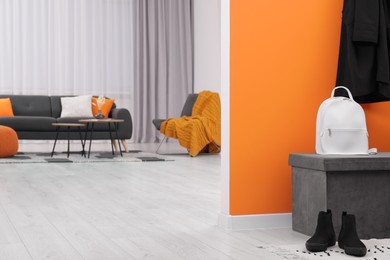 Photo of Pouf with backpack and shoes near orange wall in stylish room, space for text. Interior design