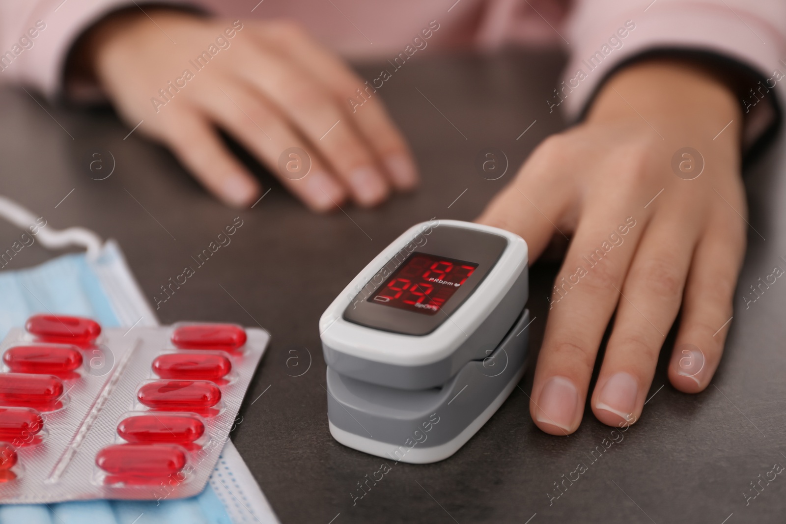 Photo of Woman measuring oxygen level with modern fingertip pulse oximeter at grey table, closeup