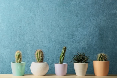 Photo of Different potted cacti on table near color background, space for text. Interior decor