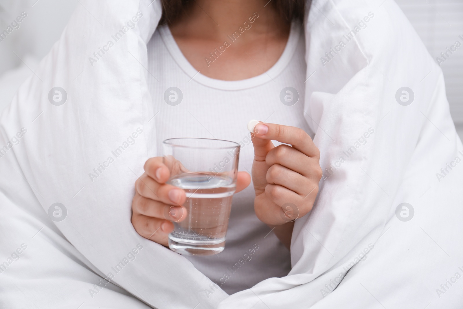 Photo of Woman holding glass of water and pill in bedroom, closeup