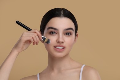 Photo of Teenage girl with makeup brush on beige background