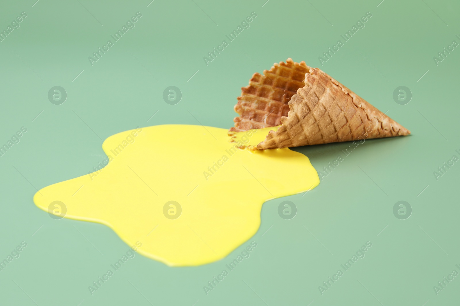 Photo of Melted ice cream and wafer cone on green background, closeup