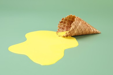 Photo of Melted ice cream and wafer cone on green background, closeup