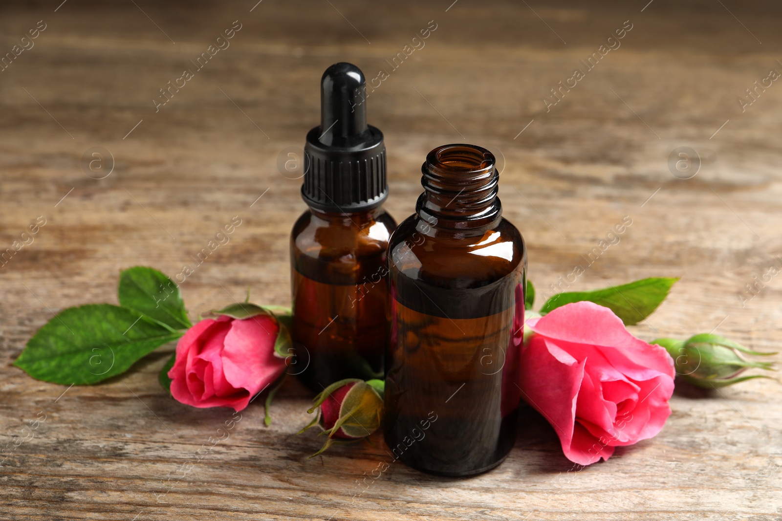 Photo of Bottles of rose essential oil and flowers on wooden table