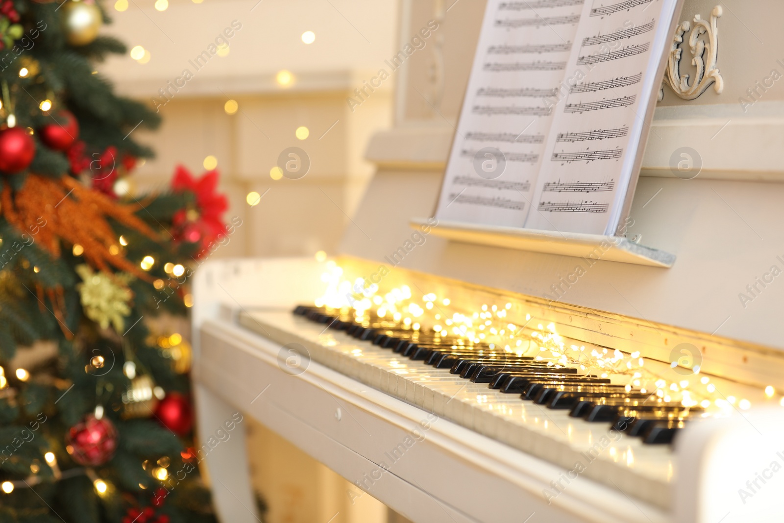 Photo of White piano with festive decor and note sheets indoors. Christmas music