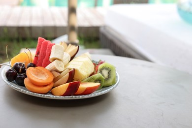 Plate with fresh fruits on table near sun lounger, space for text. Luxury resort with outdoor swimming pool