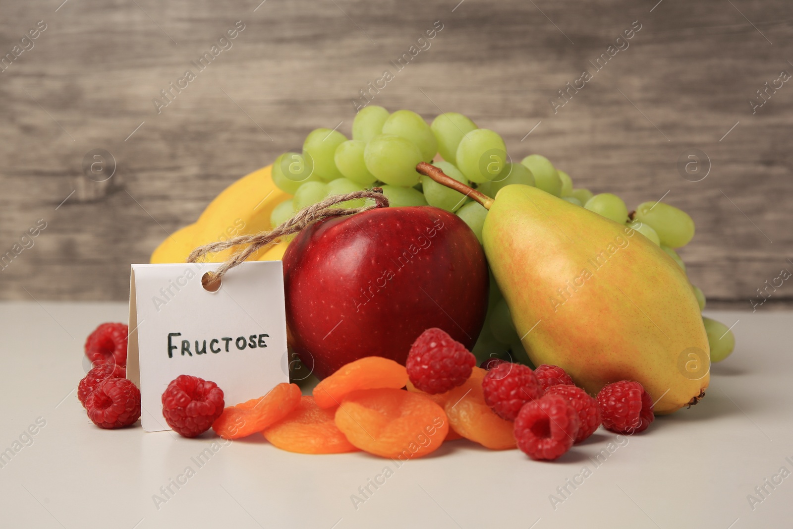 Photo of Card with word Fructose, delicious ripe fruits, raspberries and dried apricots on beige table