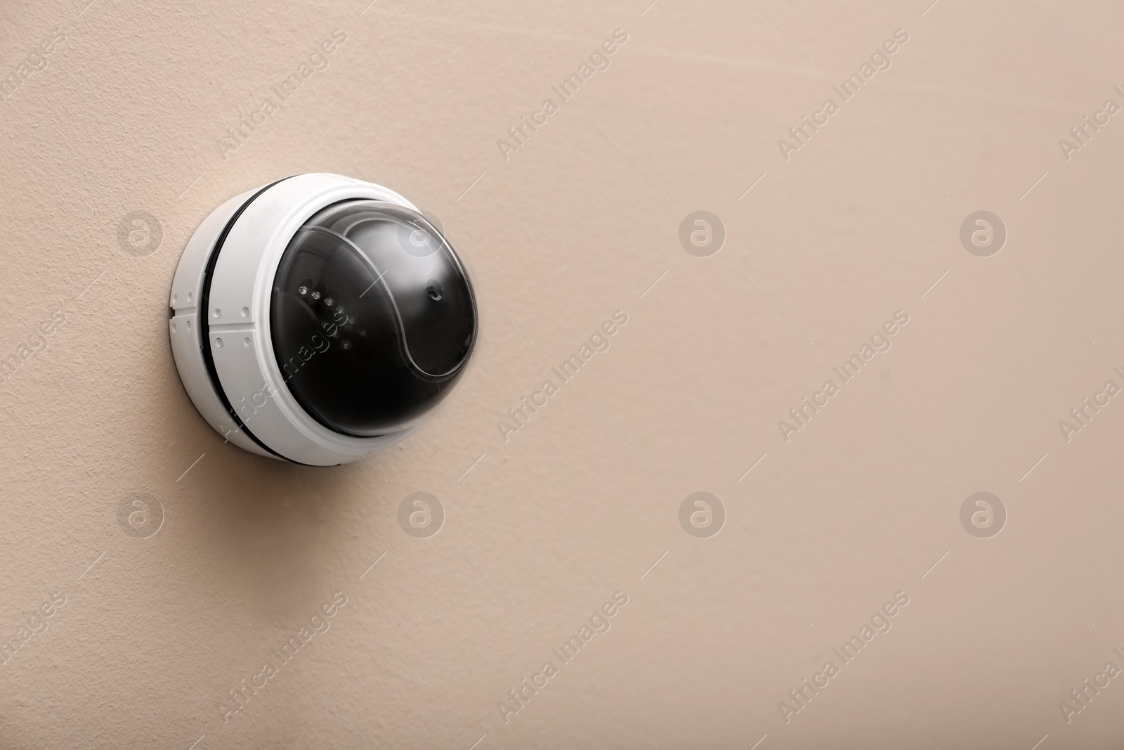 Photo of Modern CCTV security camera on beige wall. Space for text