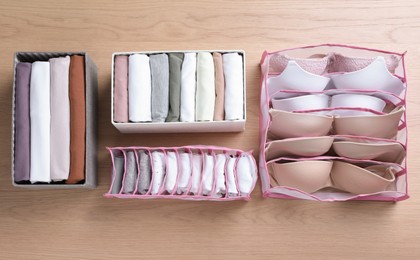 Photo of Different organizers with folded clothes and underwear on wooden background, flat lay. Vertical storage
