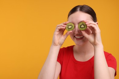 Photo of Smiling woman covering eyes with halves of kiwi on orange background, space for text