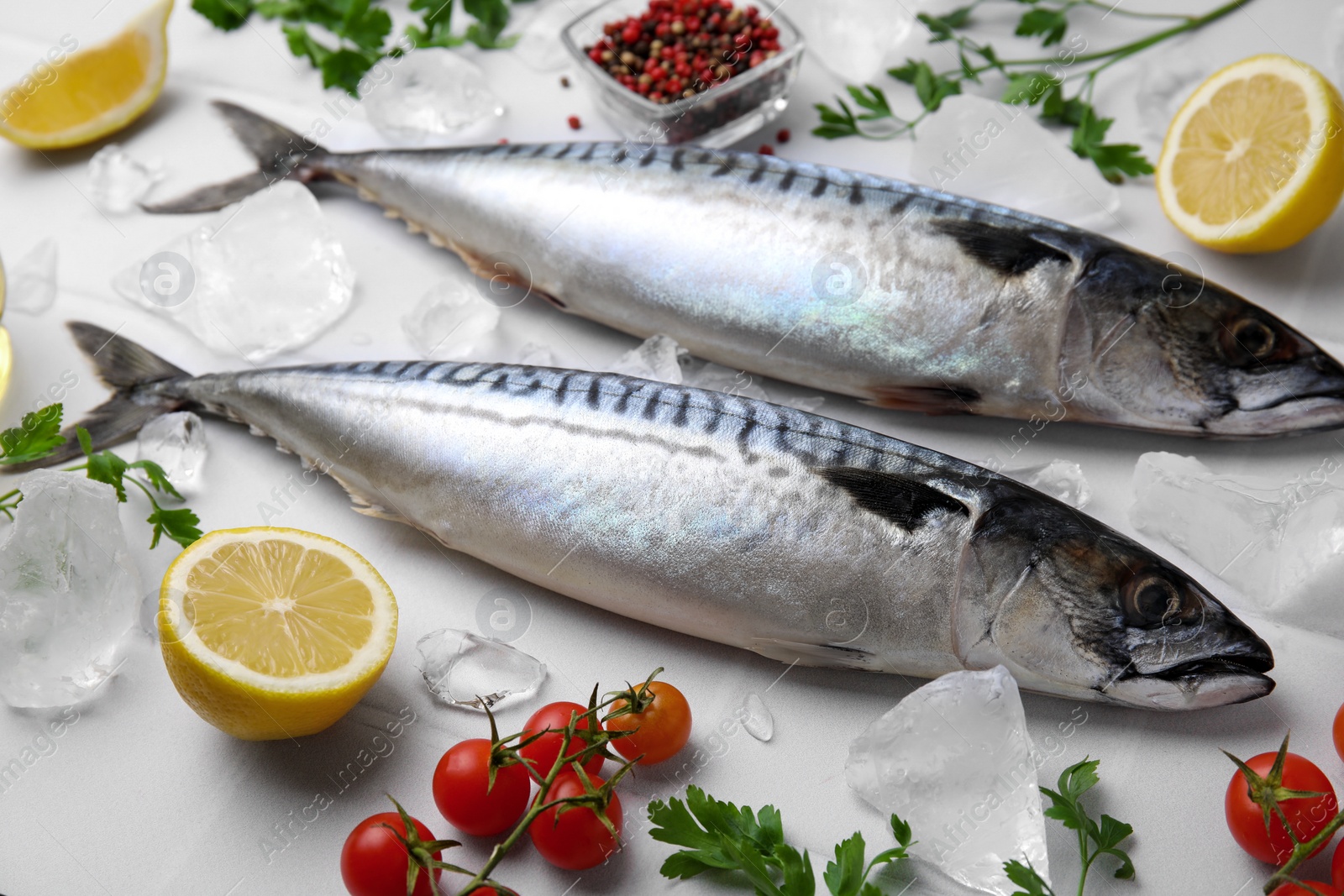 Photo of Raw mackerel, lemons and tomatoes on white table