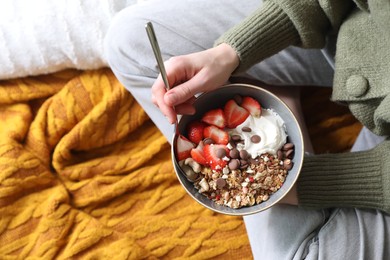 Woman eating tasty granola with chocolate chips, strawberries and yogurt indoors, top view