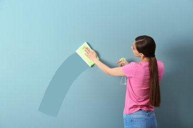 Young woman wiping color wall with rag. Cleaning service 