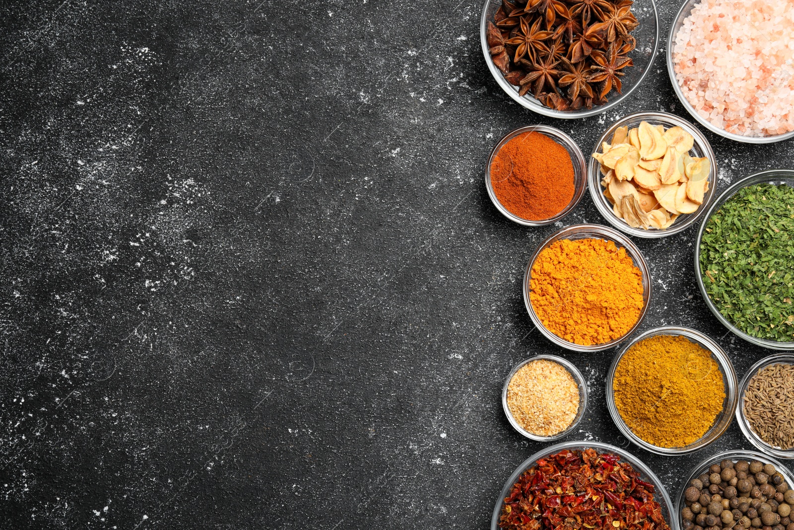 Photo of Glass bowls with different spices on grey textured table, flat lay. Space for text