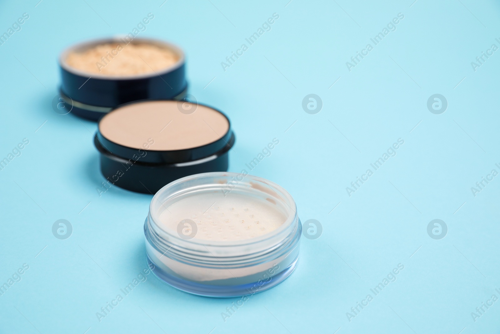 Photo of Three different face powders on light blue background, space for text