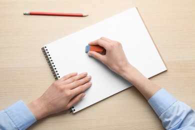 Photo of Woman erasing something in notebook at wooden table, closeup