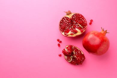 Whole and cut fresh pomegranates on pink background, flat lay. Space for text