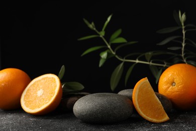 Photo of Tasty fresh oranges, stones and leaves on black table, closeup