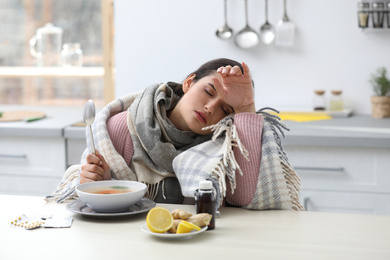 Photo of Sick young woman eating soup to cure flu at table in kitchen
