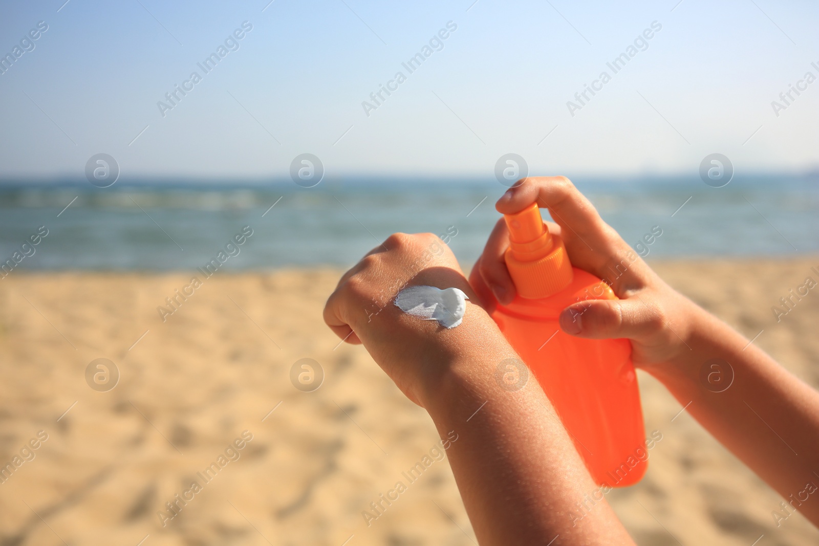 Photo of Child applying sunscreen near sea, closeup. Space for text. Sun protection care