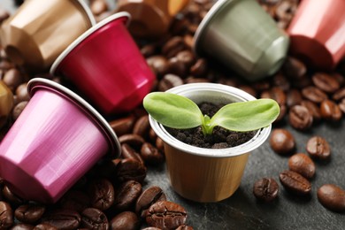 Photo of Coffee capsules with seedling and beans on black table, closeup