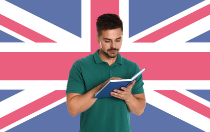 Image of Handsome young man reading book and flag of Great Britain on wall. Learning English