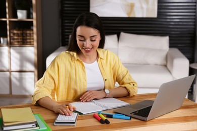 Young woman counting on calculator during webinar at table in room