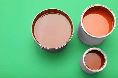 Photo of Cans of orange paint on green background, top view