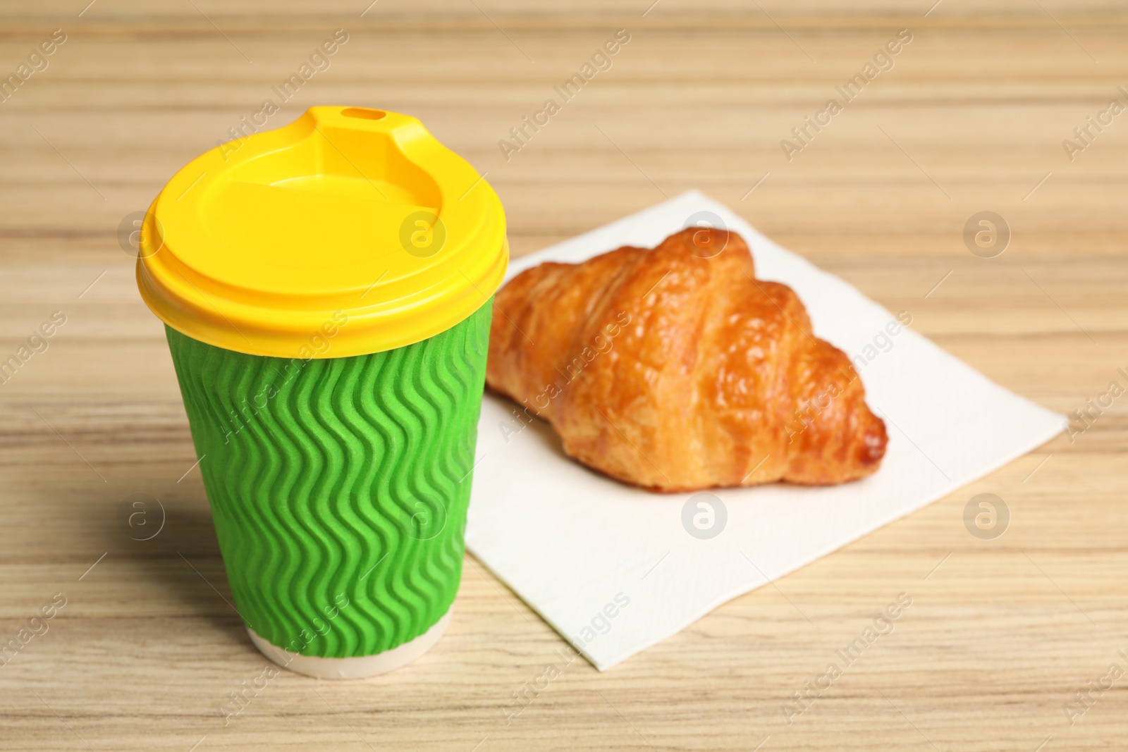 Photo of Paper cup with coffee and croissant on wooden table