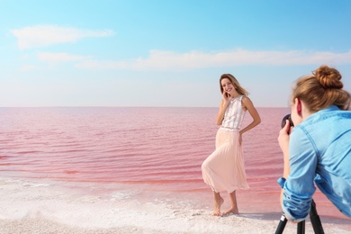 Female photographer taking pictures of model near pink lake