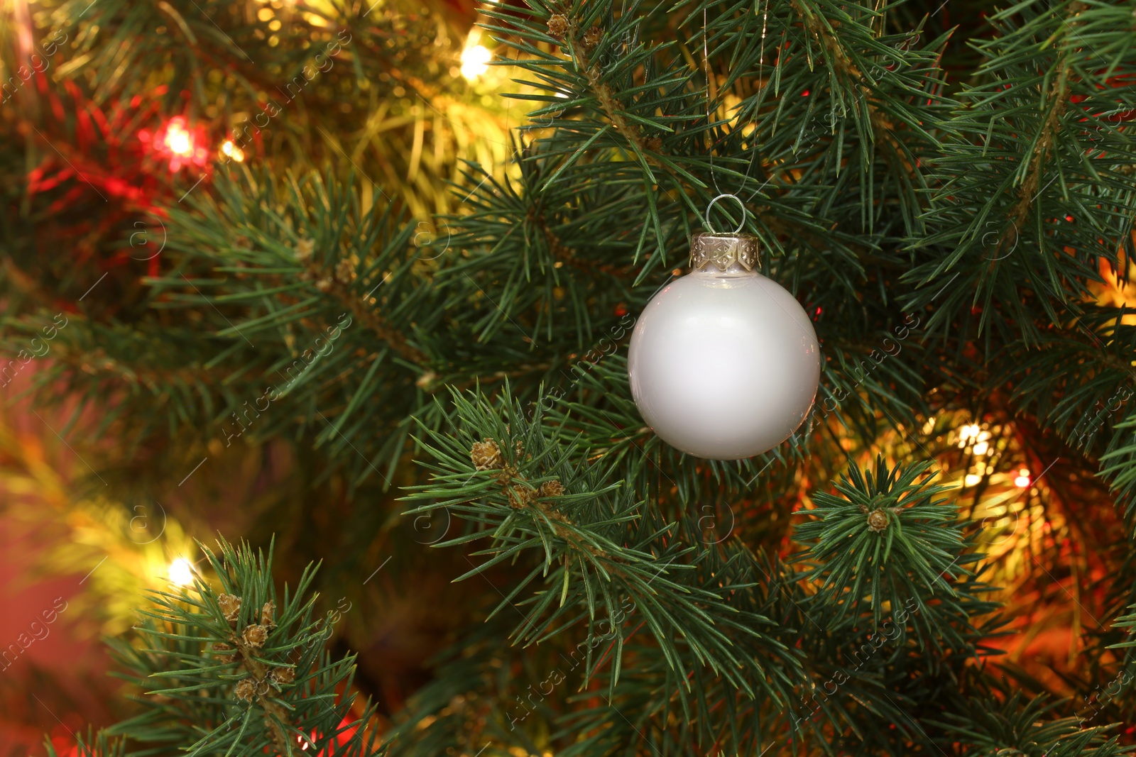 Photo of Glowing fairy lights and beautiful bauble on Christmas tree, closeup