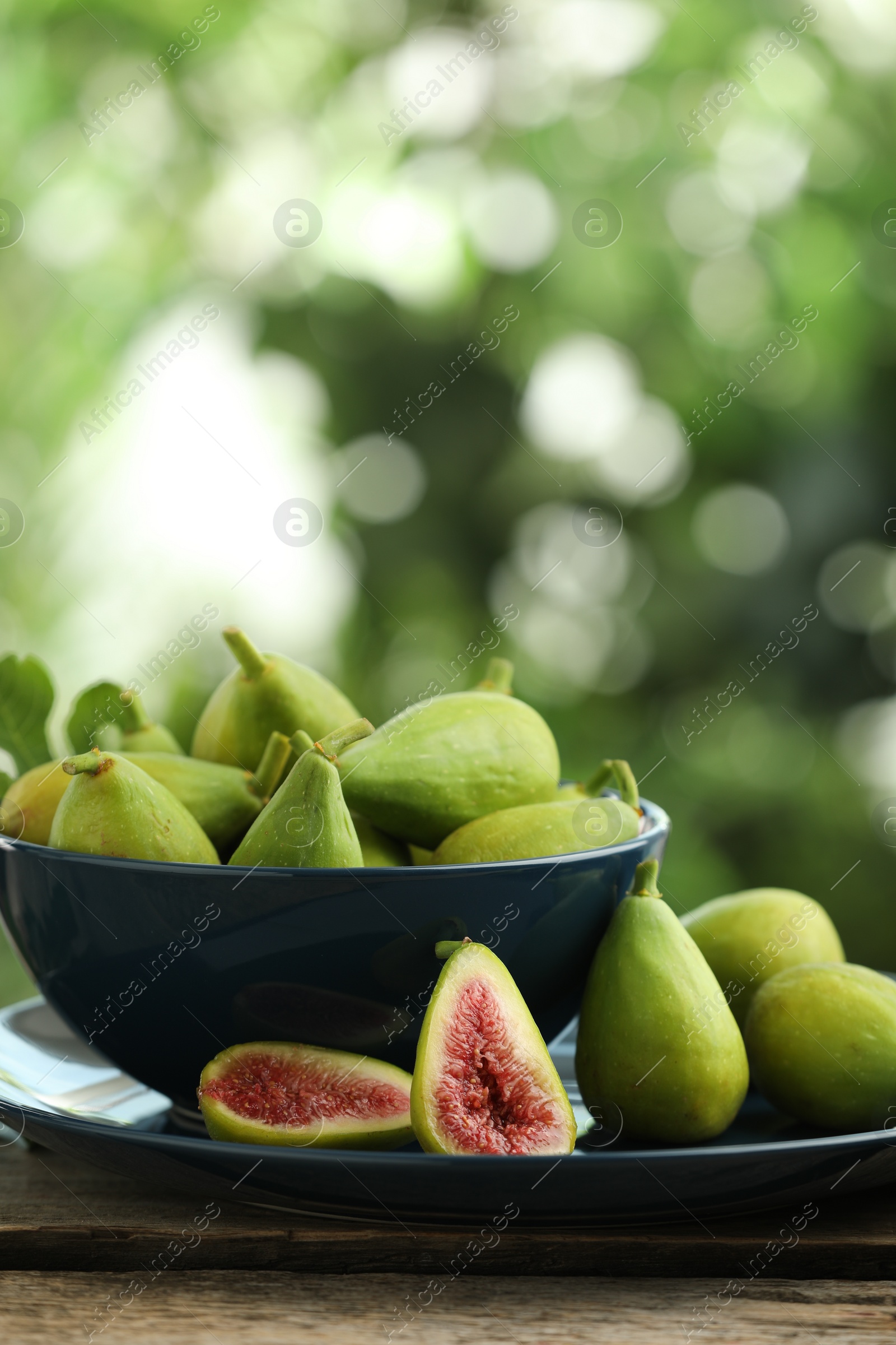 Photo of Cut and whole green figs on wooden table against blurred background, space for text