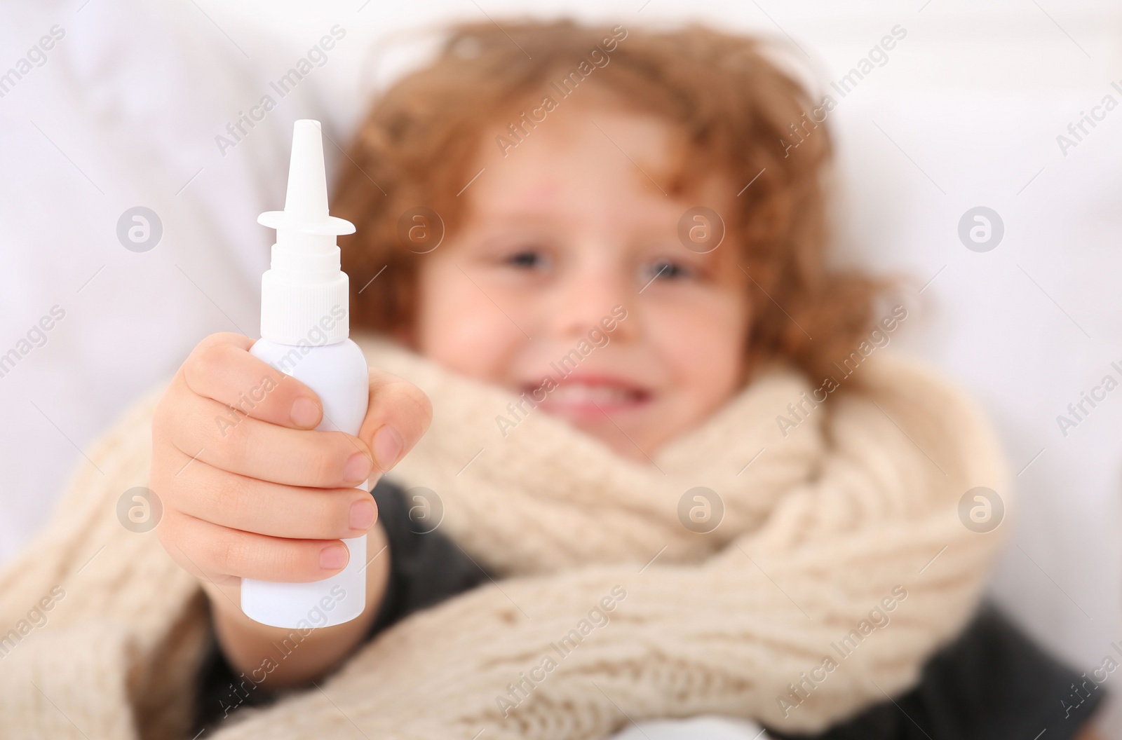 Photo of Cute little boy showing nasal spray on bed, focus on hand