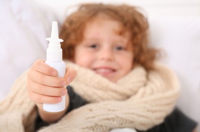 Cute little boy showing nasal spray on bed, focus on hand