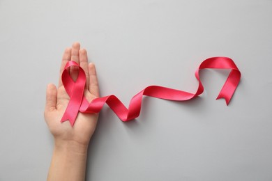 Woman holding pink ribbon on light grey background, top view. Breast cancer awareness concept