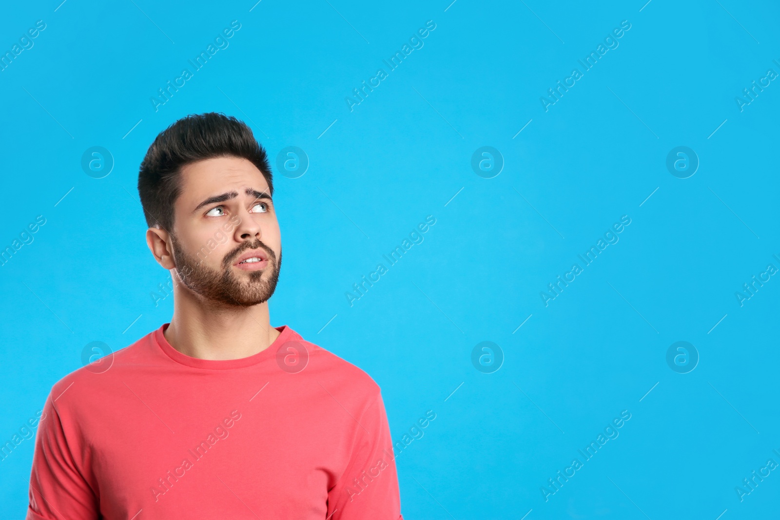 Photo of Pensive young man on light blue background, space for text. Thinking about difficult question