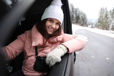 Photo of Young woman driving car and looking out of window on road. Winter vacation