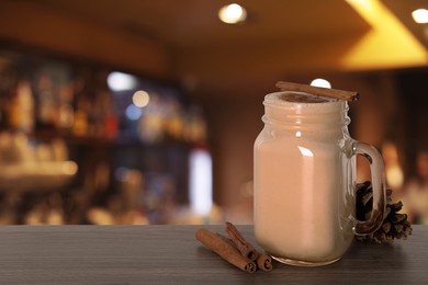 Image of Mason jar with delicious eggnog, cinnamon sticks and cone on wooden table in bar, space for text