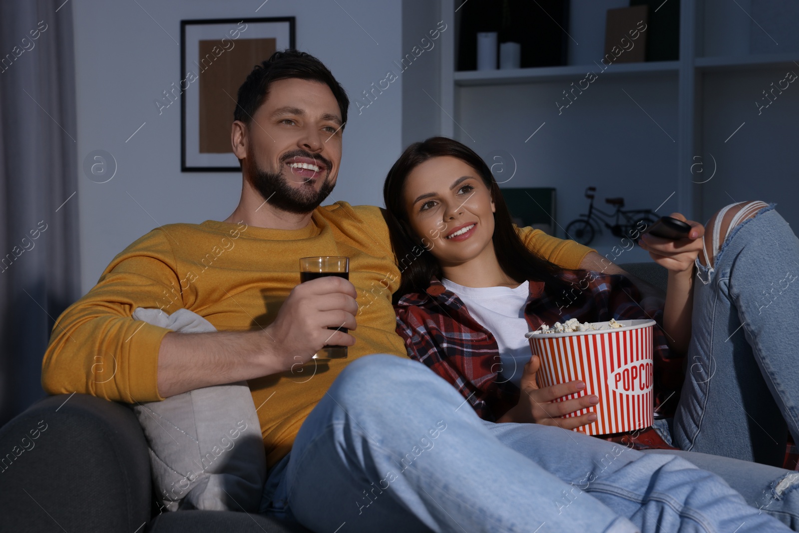 Photo of Happy couple with popcorn watching TV at home in evening