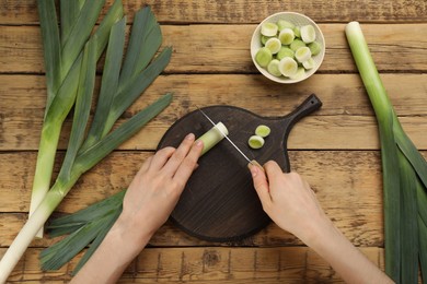 Photo of Woman cutting leek at wooden table, top view