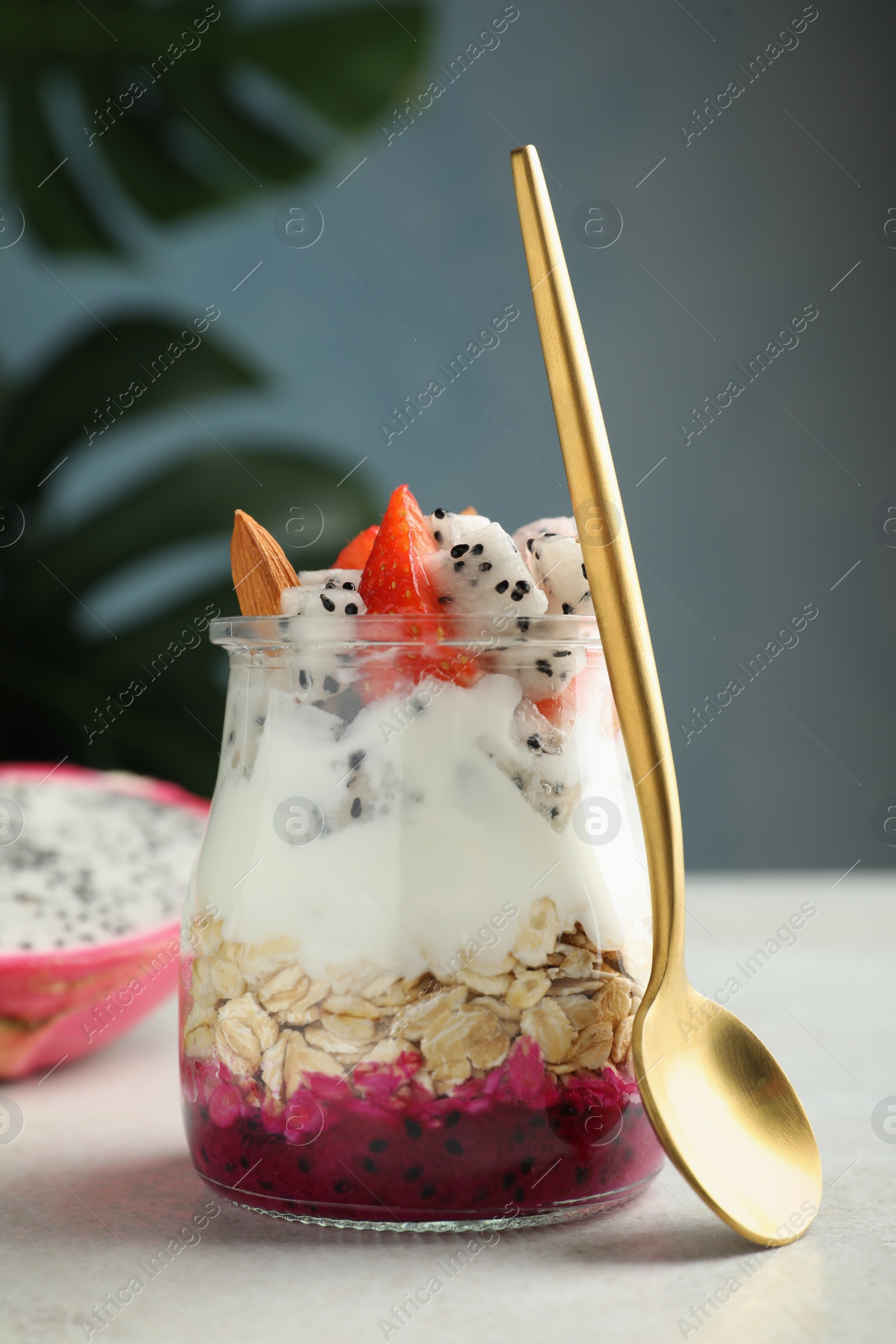 Photo of Glass jar of granola with pitahaya, yogurt and strawberries on white table