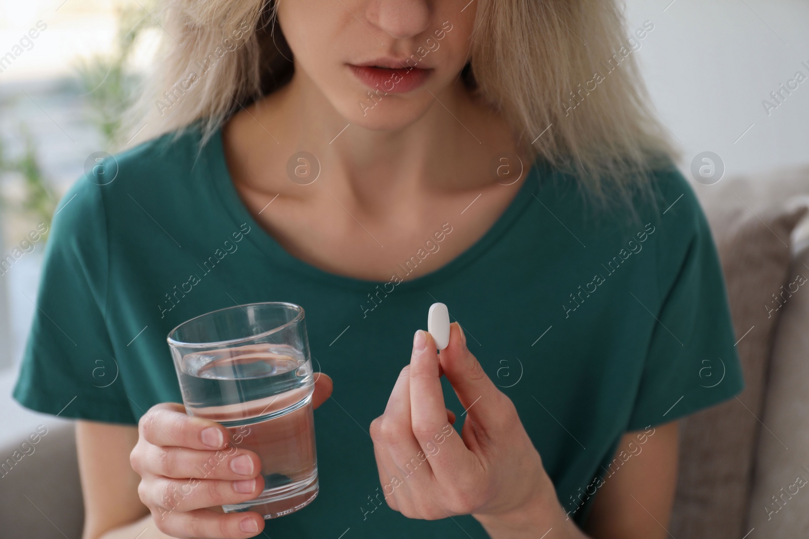 Photo of Young woman with abortion pill and glass of water at home, closeup