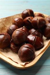 Photo of Fresh edible sweet chestnuts in serving plate on light blue wooden table