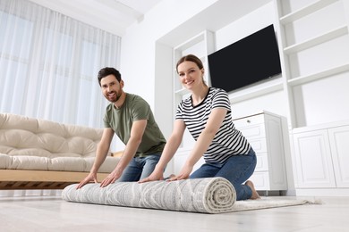 Photo of Smiling couple unrolling carpet with beautiful pattern on floor in room