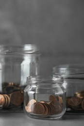 Glass jars with coins on grey table, closeup