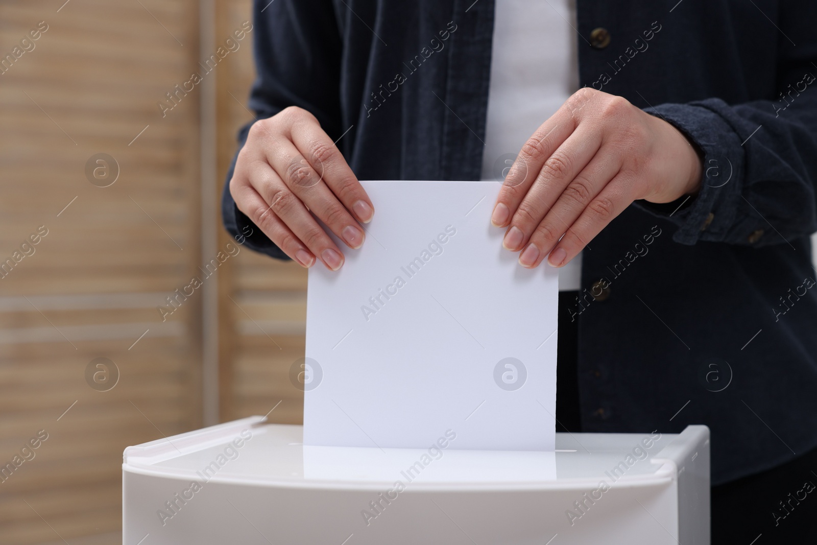 Photo of Woman putting her vote into ballot box on blurred background, closeup