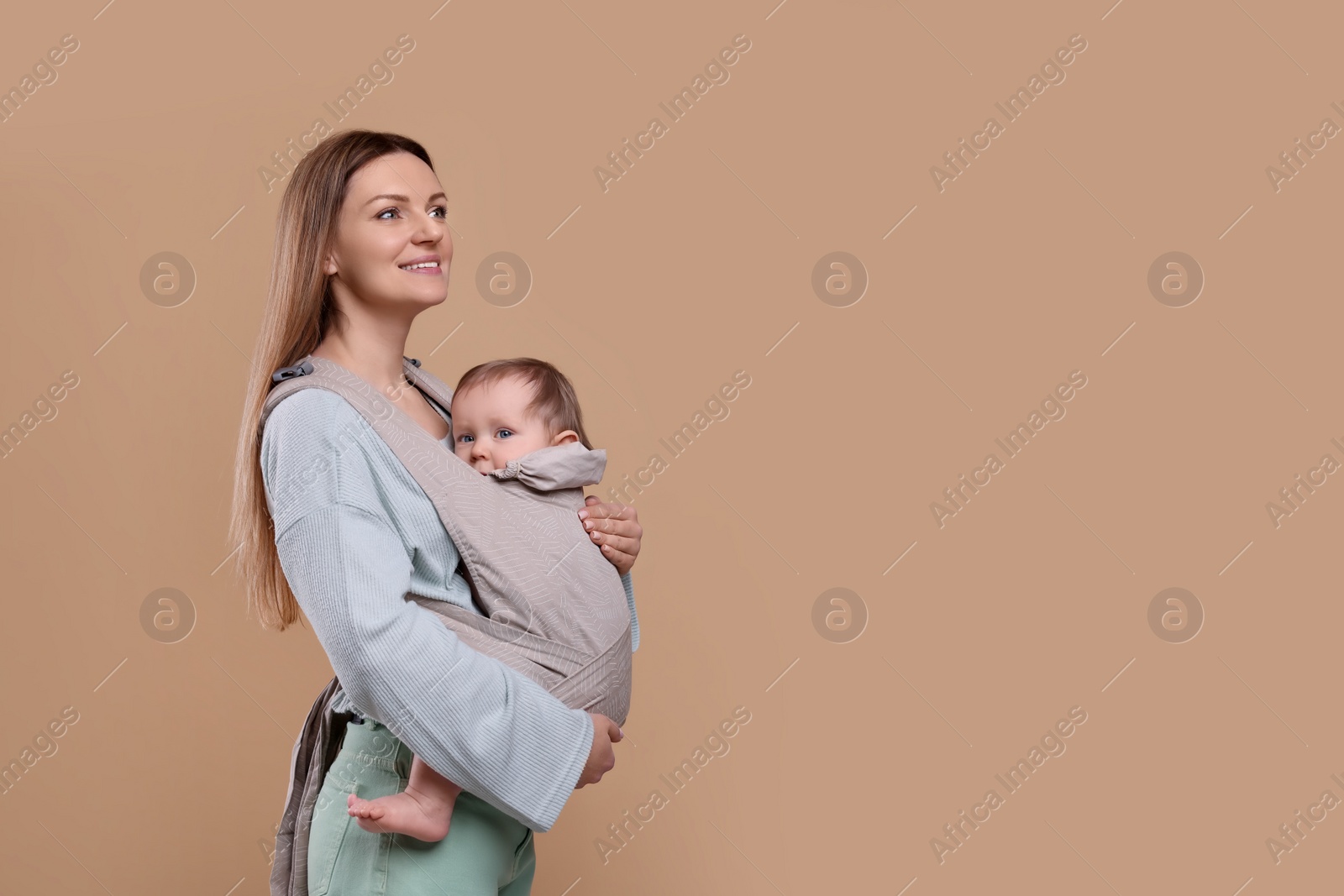 Photo of Mother holding her child in sling (baby carrier) on light brown background. Space for text