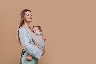 Photo of Mother holding her child in sling (baby carrier) on light brown background. Space for text