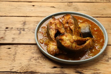 Photo of Tasty fish curry on wooden table, closeup. Space for text. Indian cuisine