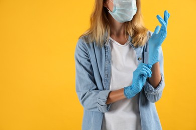 Young woman in protective mask putting on medical gloves against yellow background, closeup